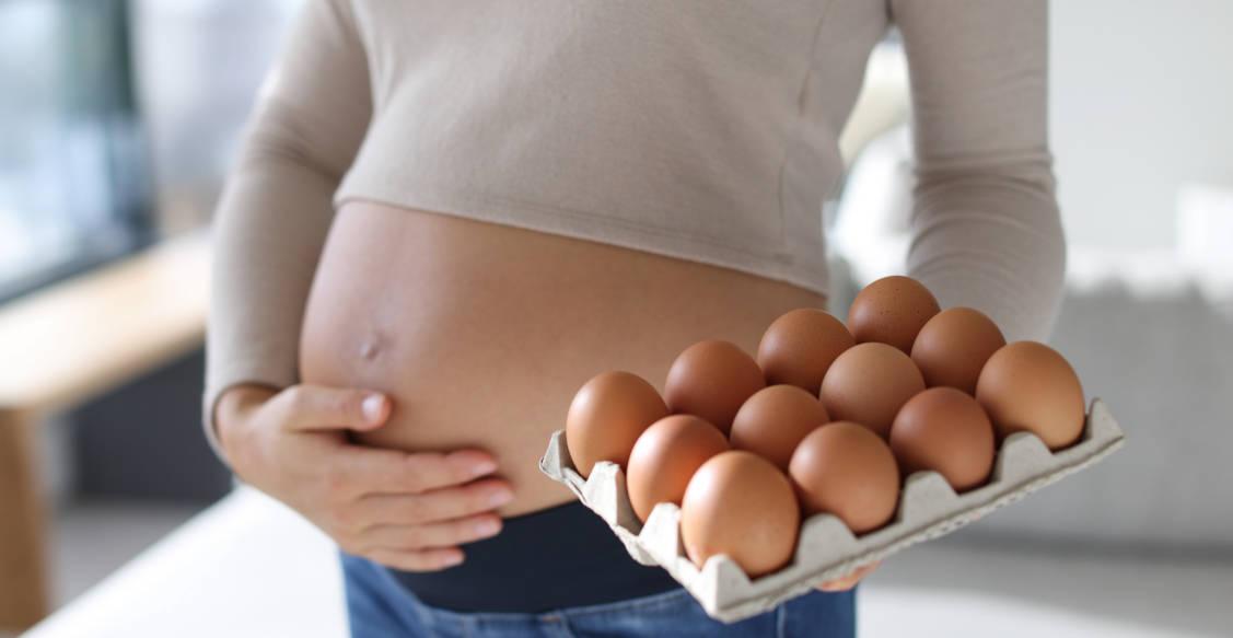 Seorang ibu hamil sedang memegang satu kotak berisi telur yang tinggi protein