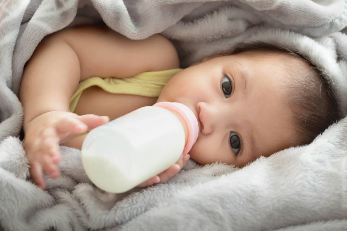 Bayi sedang minum susu dalam botol dengan memegang sendiri 